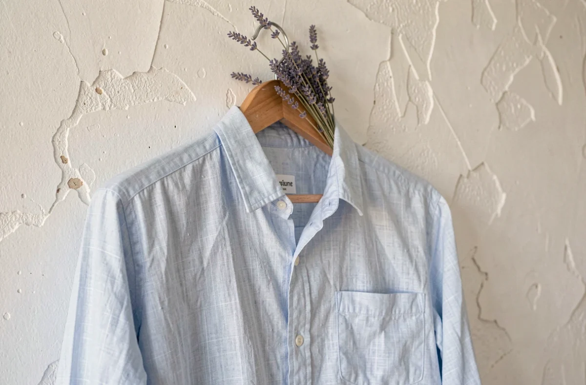 Chemise en lin bleu clair suspendue à un cintre en bois contre un mur blanchi à la chaux en Provence